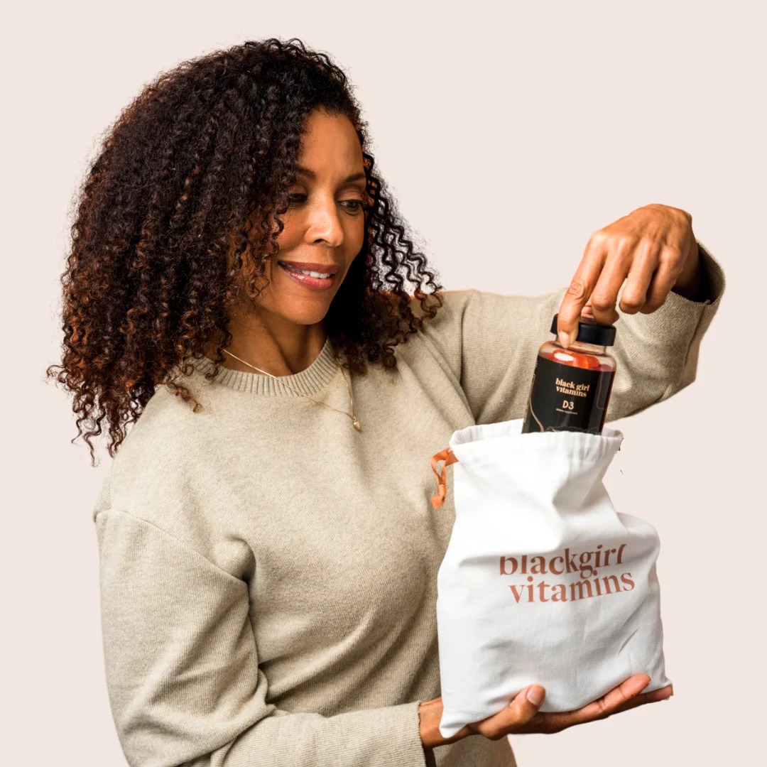 A woman with curly hair pulling a bottle out of a white Black Girl Vitamins bag