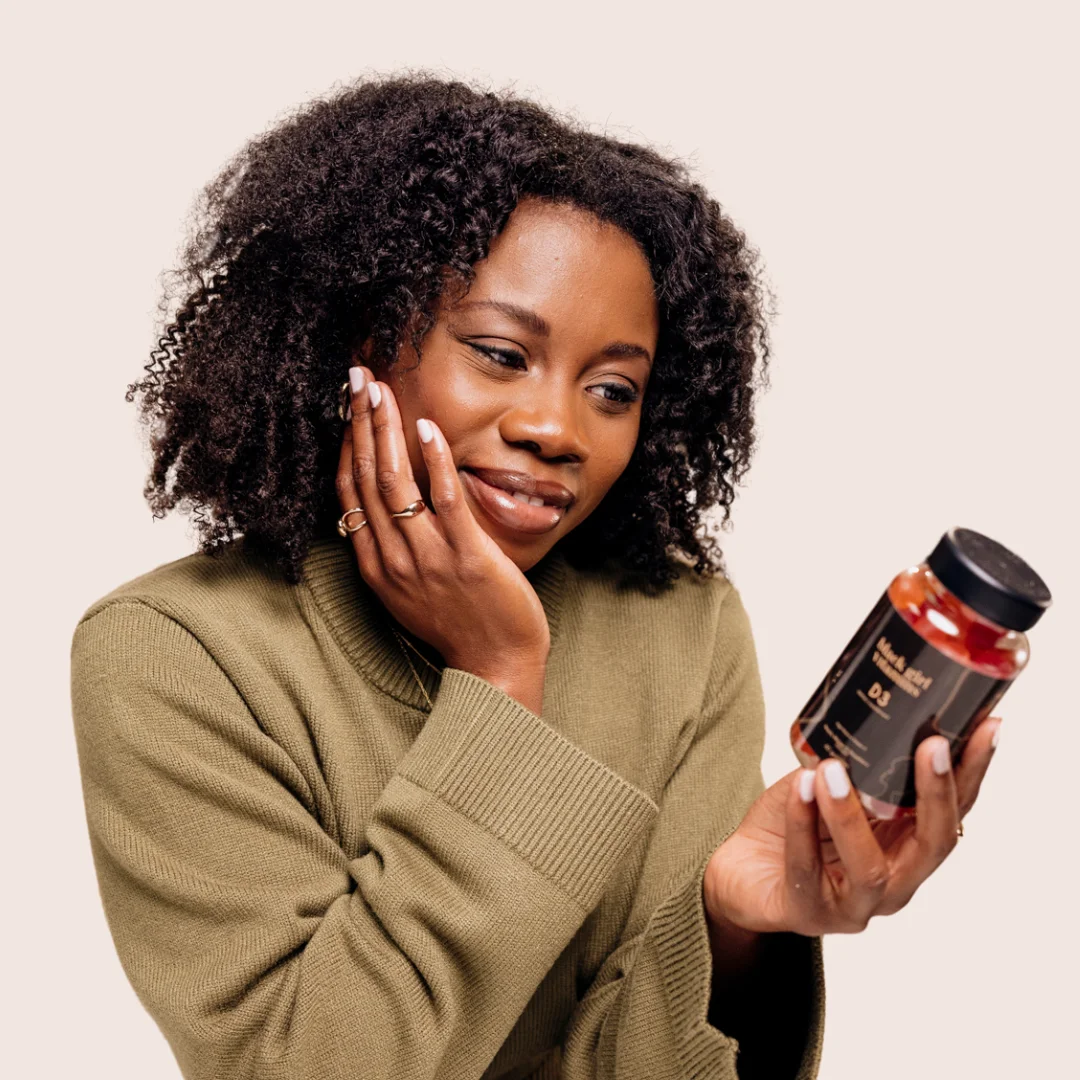 A woman with natural hair looking at a bottle of vitamins in her hand