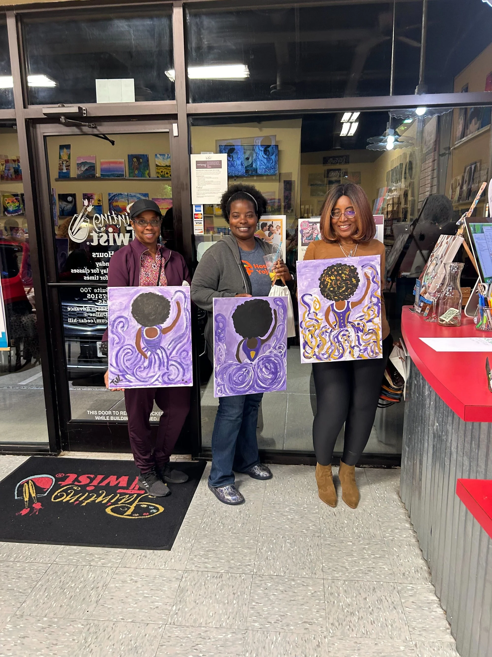 Women standing in front of a painting studio holding their finished canvases